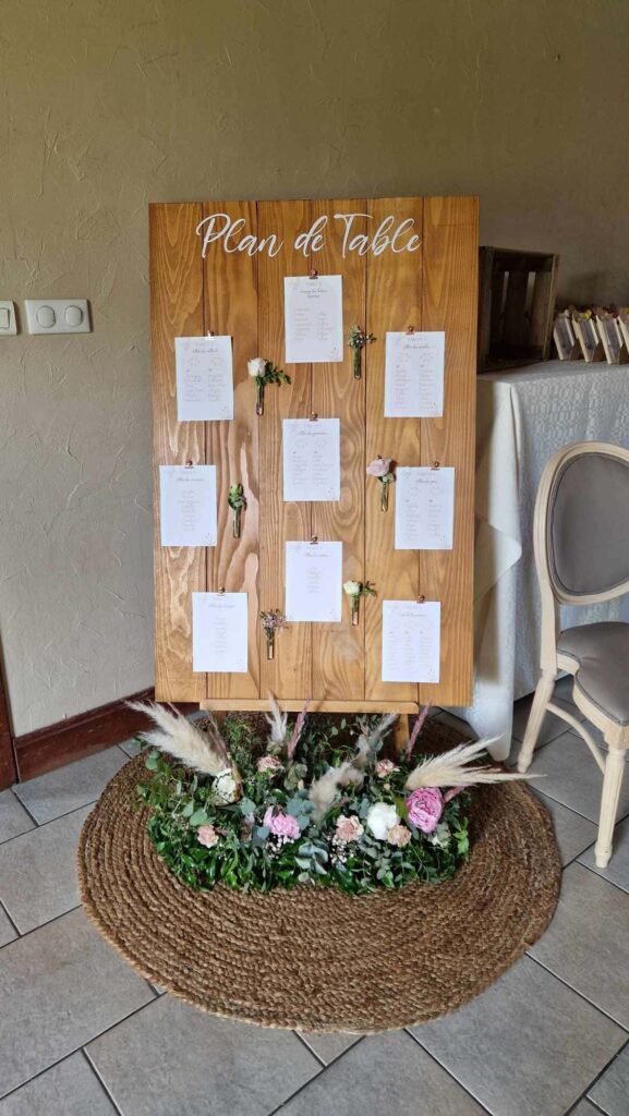 Plan de table personnalisé avec petites fioles de fleurs, composition florale de pivoines, roses, oeillets, pampa, eucalyptus et tapis de jute