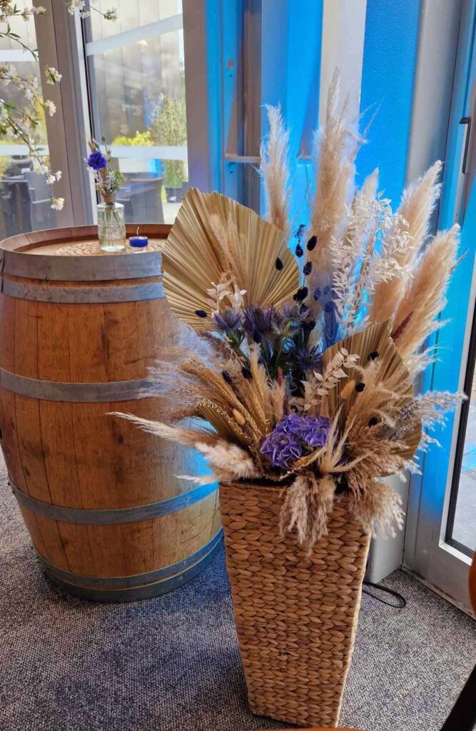 Compositions de fleurs séchées dans un pot en osier comprenant des épis de blé, des fleurs séchées, blanches beiges et bleues pour un mariage guinguette avec Nature Event